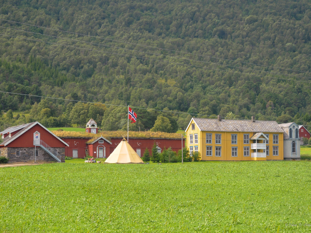 avstandbilde av en gammel gård med gult hovedhus og røde fjøs